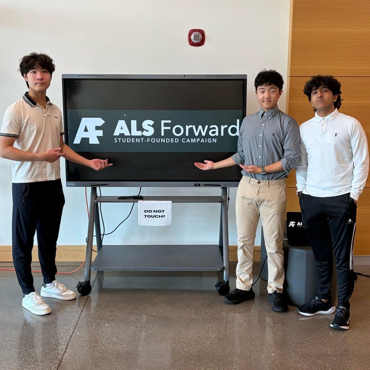 Three ALS Forward students beside a screen showing the ALS Forward logo